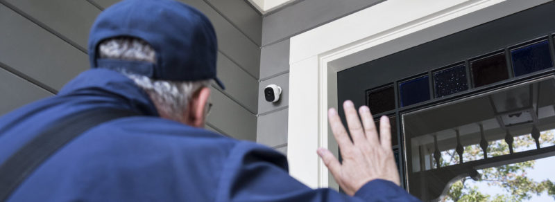 delivery man walking to a front door and waving to a outdoor home security camera